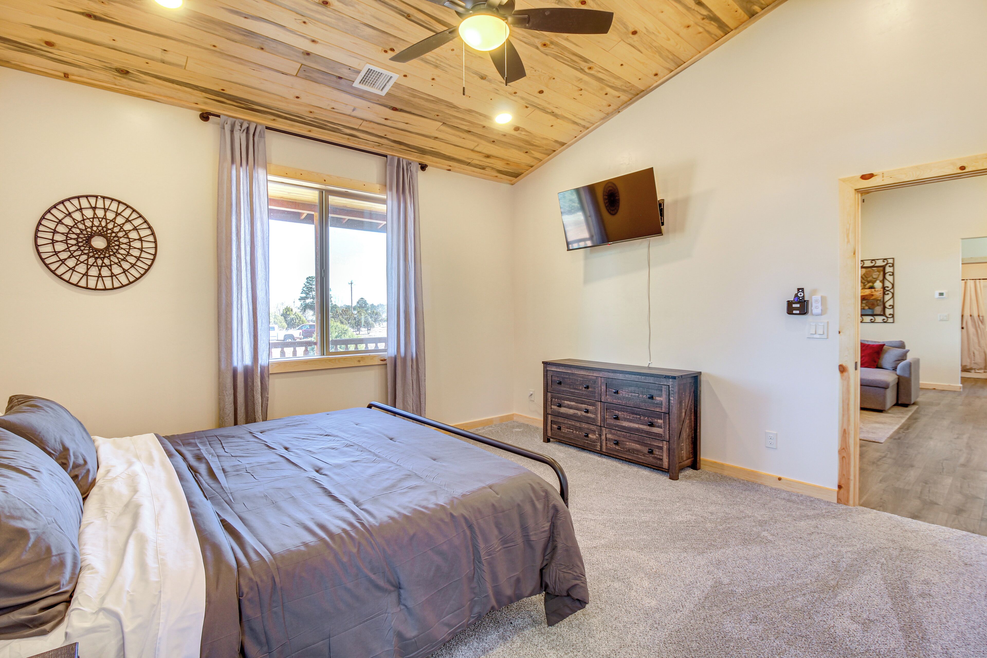 A bedroom with a bed, a ceiling fan, a TV mounted on the wall, and a window with curtains.