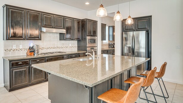 A modern kitchen with dark cabinets, stainless steel appliances, and a large island with bar stools. - Rio Bravo Country Club Home in Bakersfield w/ Pool (Bakersfield)