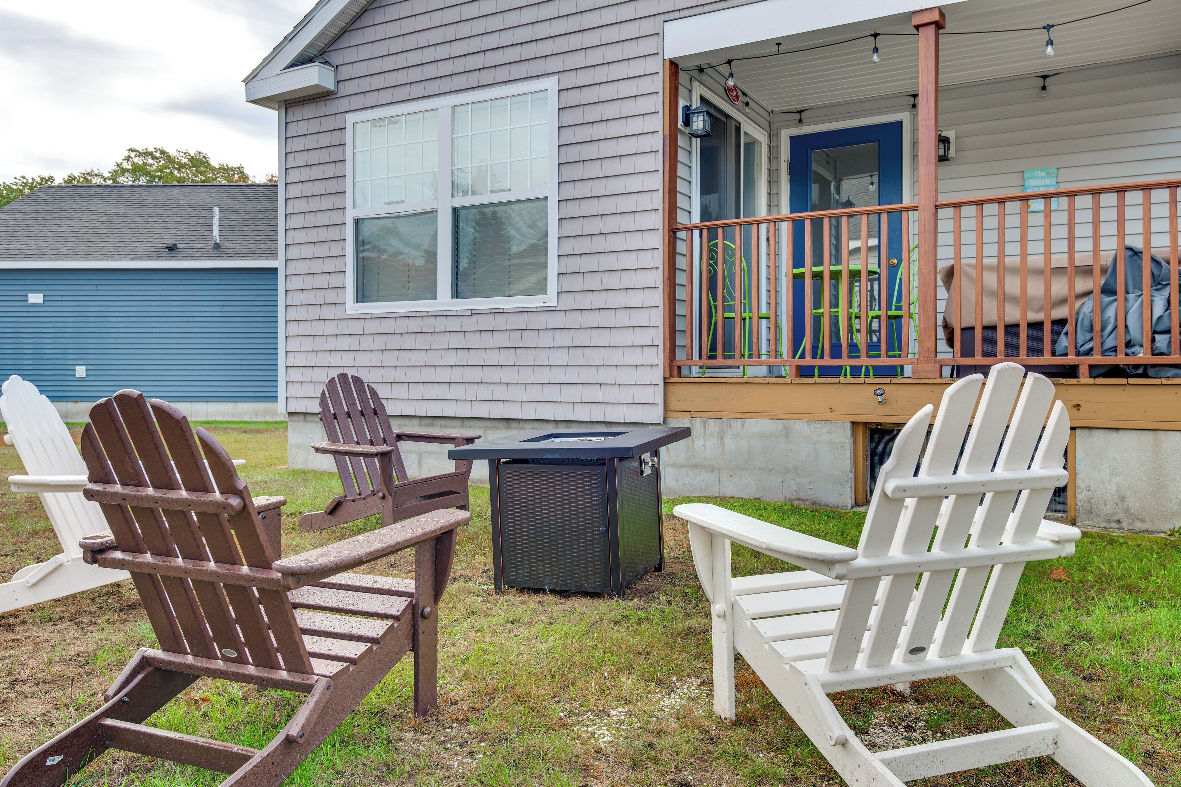 Una casa con porche, dos sillas Adirondack y una mesa pequeña.