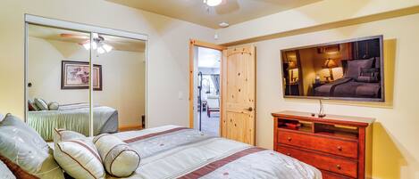 A bedroom with a bed, dresser, mirror, ceiling fan, and a door leading to another room.