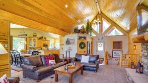 A spacious living area with a wooden ceiling, leather sofas, a coffee table, and a stone fireplace.