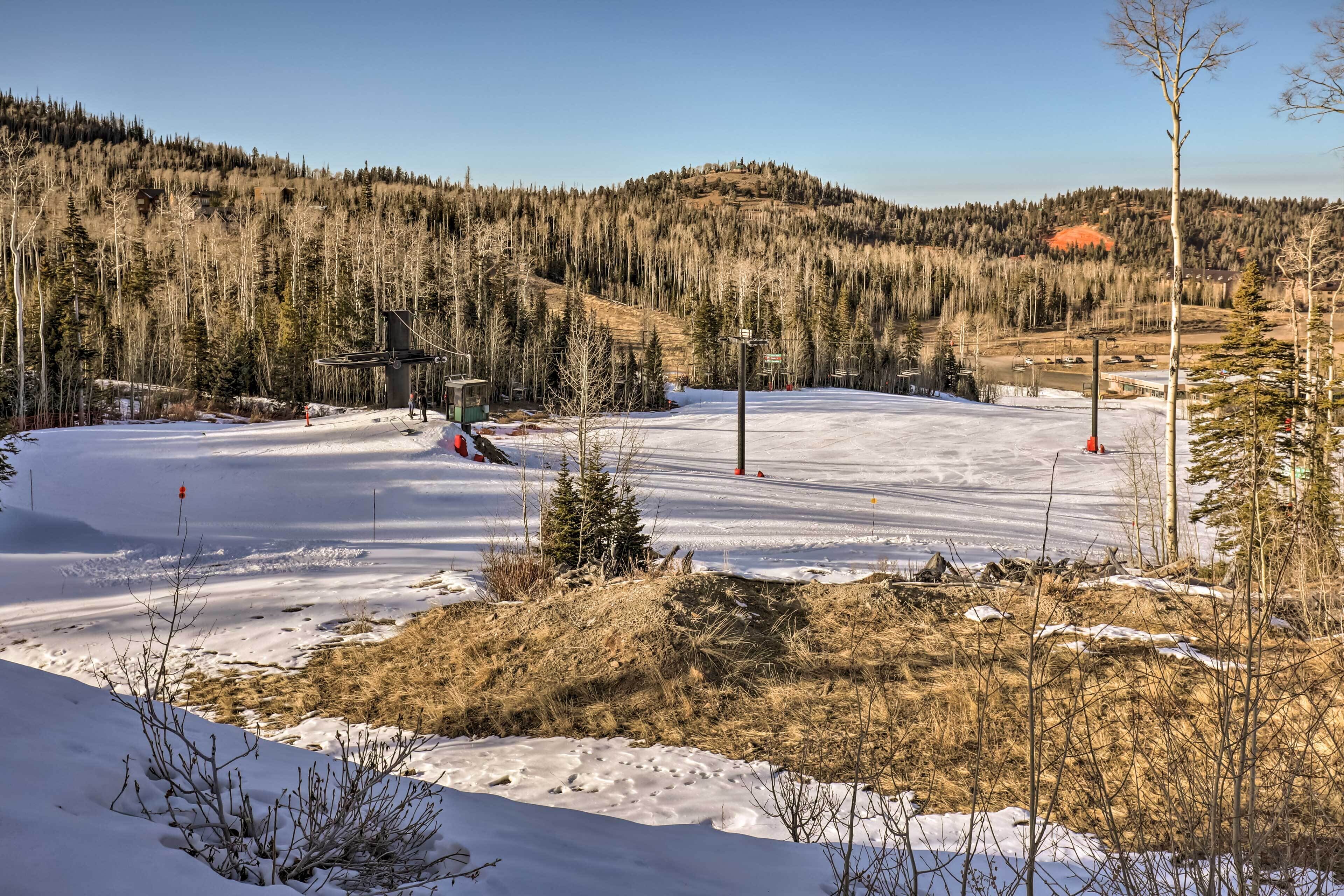 A snowy landscape with a ski lift and a forested hill in the background.