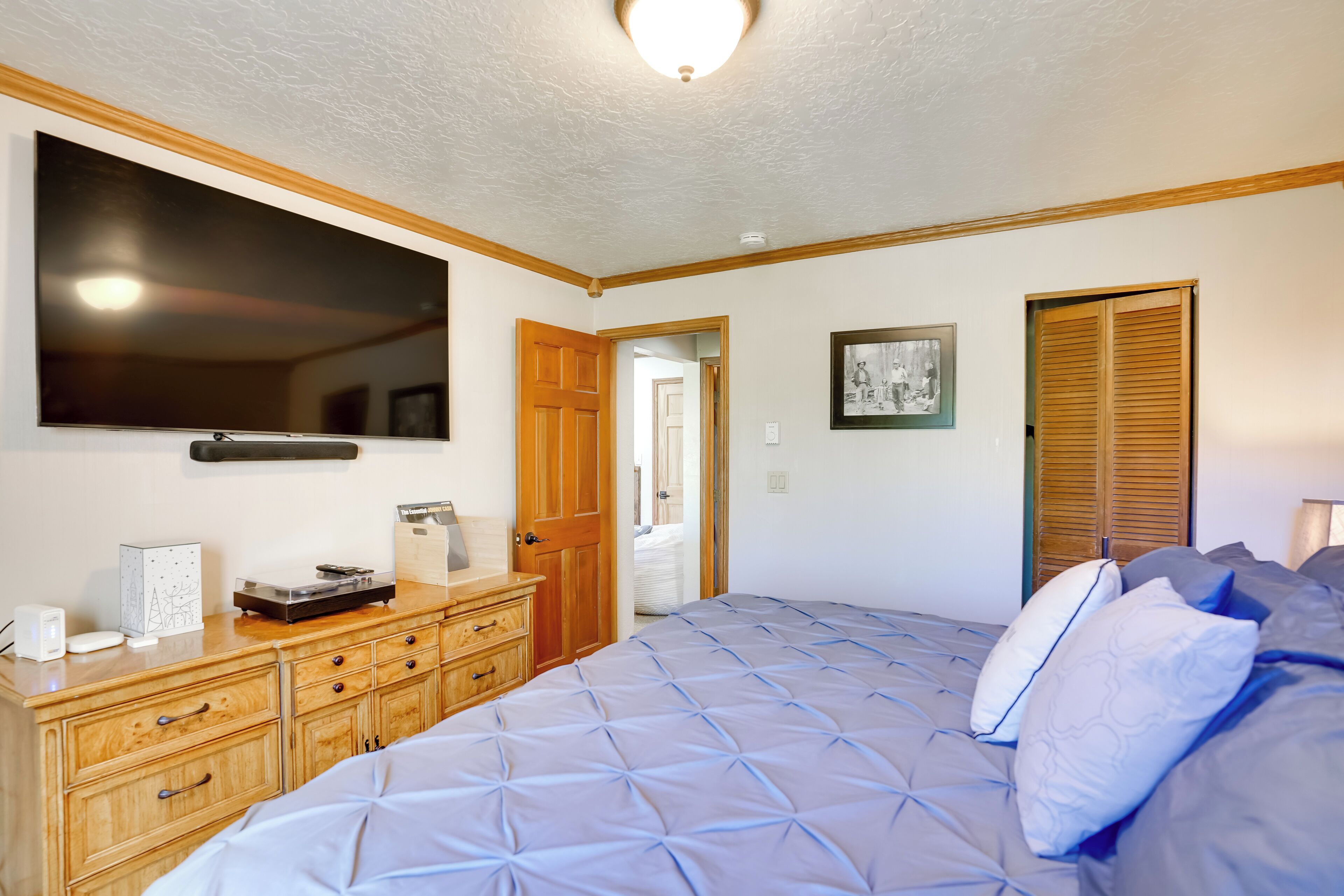 Een slaapkamer met een groot bed, een houten dressoir en een flatscreen televisie aan de muur.