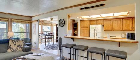 A modern kitchen with wooden cabinets, a bar area with stools, and a dining area with a round table and chairs.