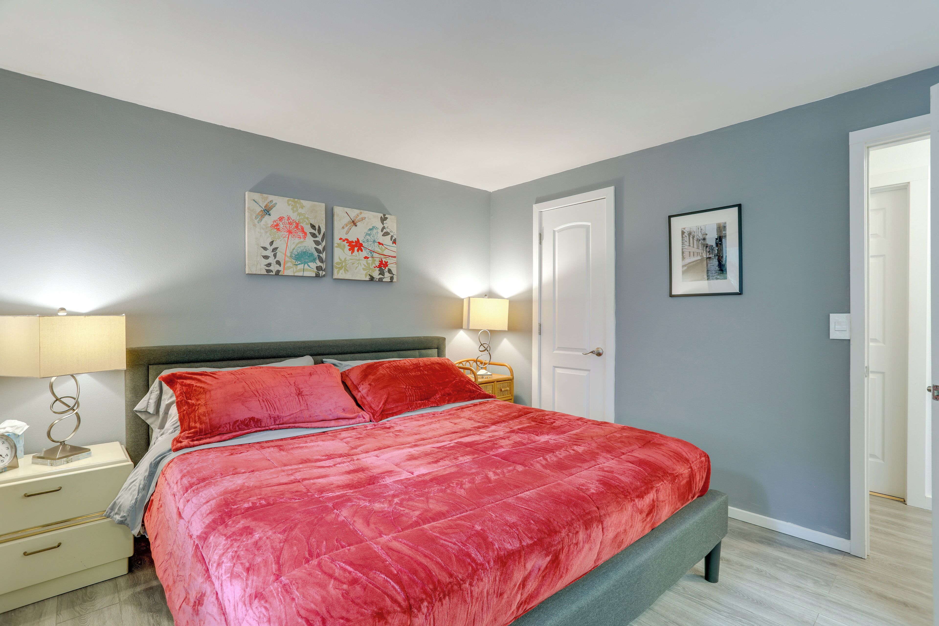 A bedroom with a large bed, two bedside tables, a nightstand, and a door.