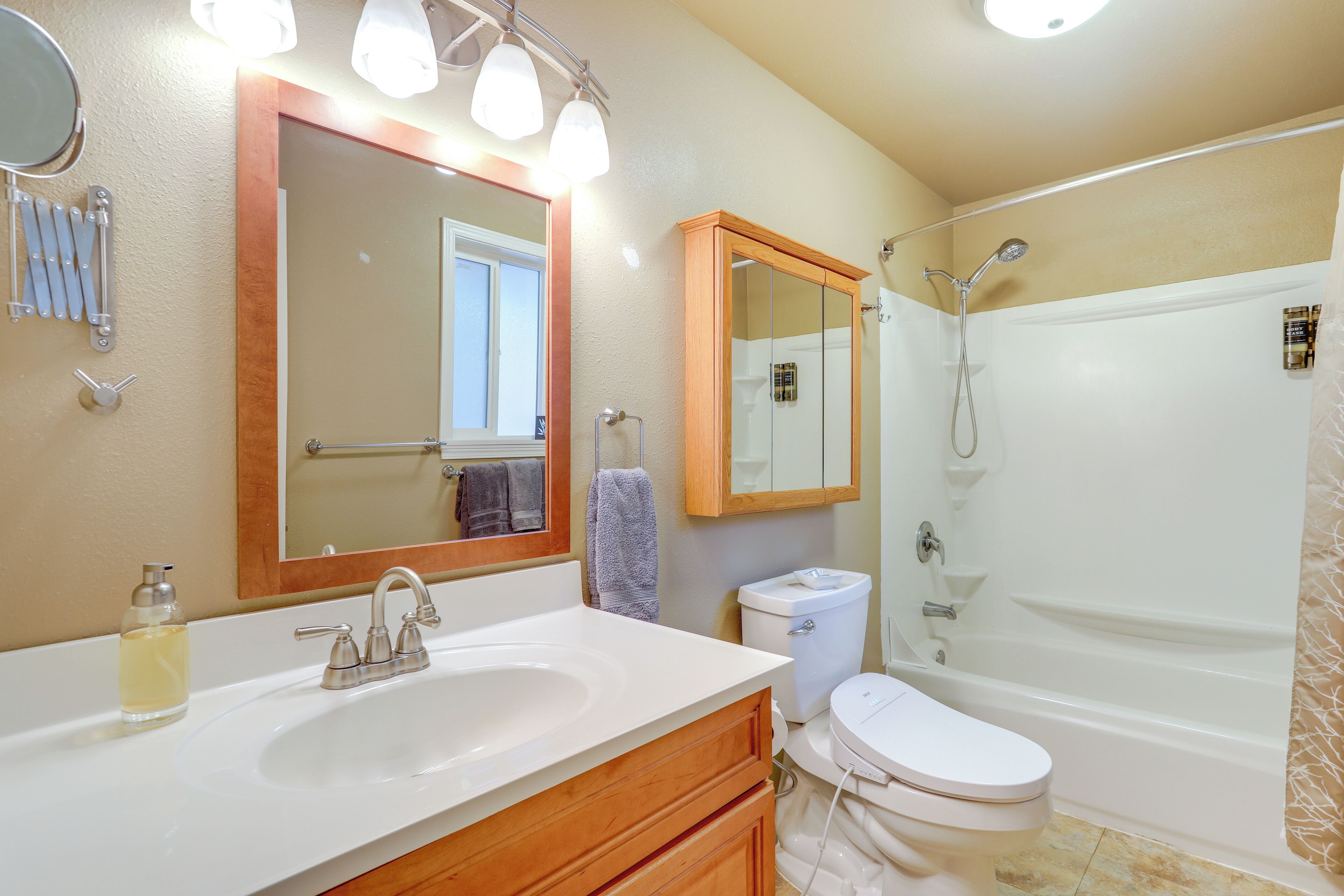 A bathroom with a white sink, wooden vanity, a mirror, a toilet, and a bathtub.