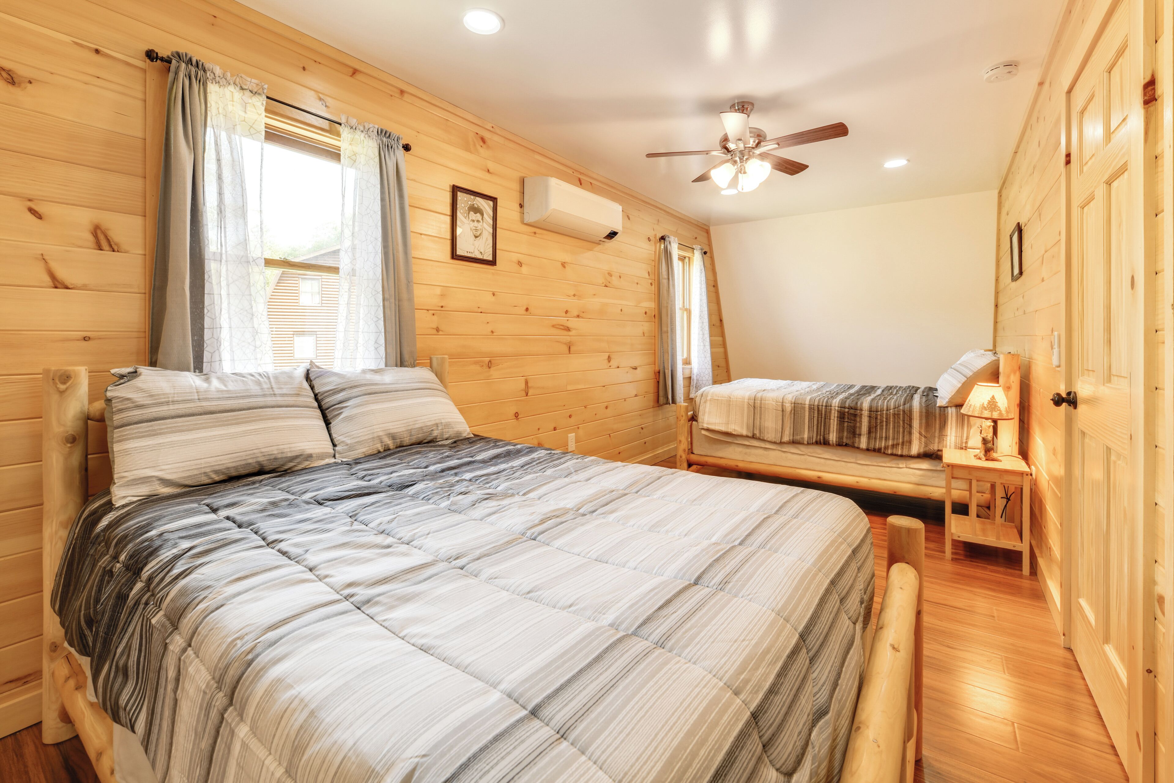 A wooden-paneled room with two beds, a ceiling fan, and an air conditioning unit.