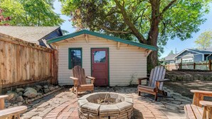 A wooden cabin with a fire pit in the center, surrounded by stone-paved patio and wooden chairs. - Willamette Valley Getaway w/ Backyard Firepit  (Newberg)