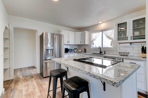 A modern kitchen with white cabinets, a stainless steel refrigerator, a granite countertop, and two black bar stools.