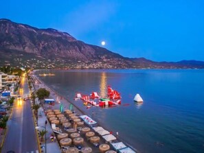 A coastal town with a marina, beach umbrellas, and a mountain in the background.