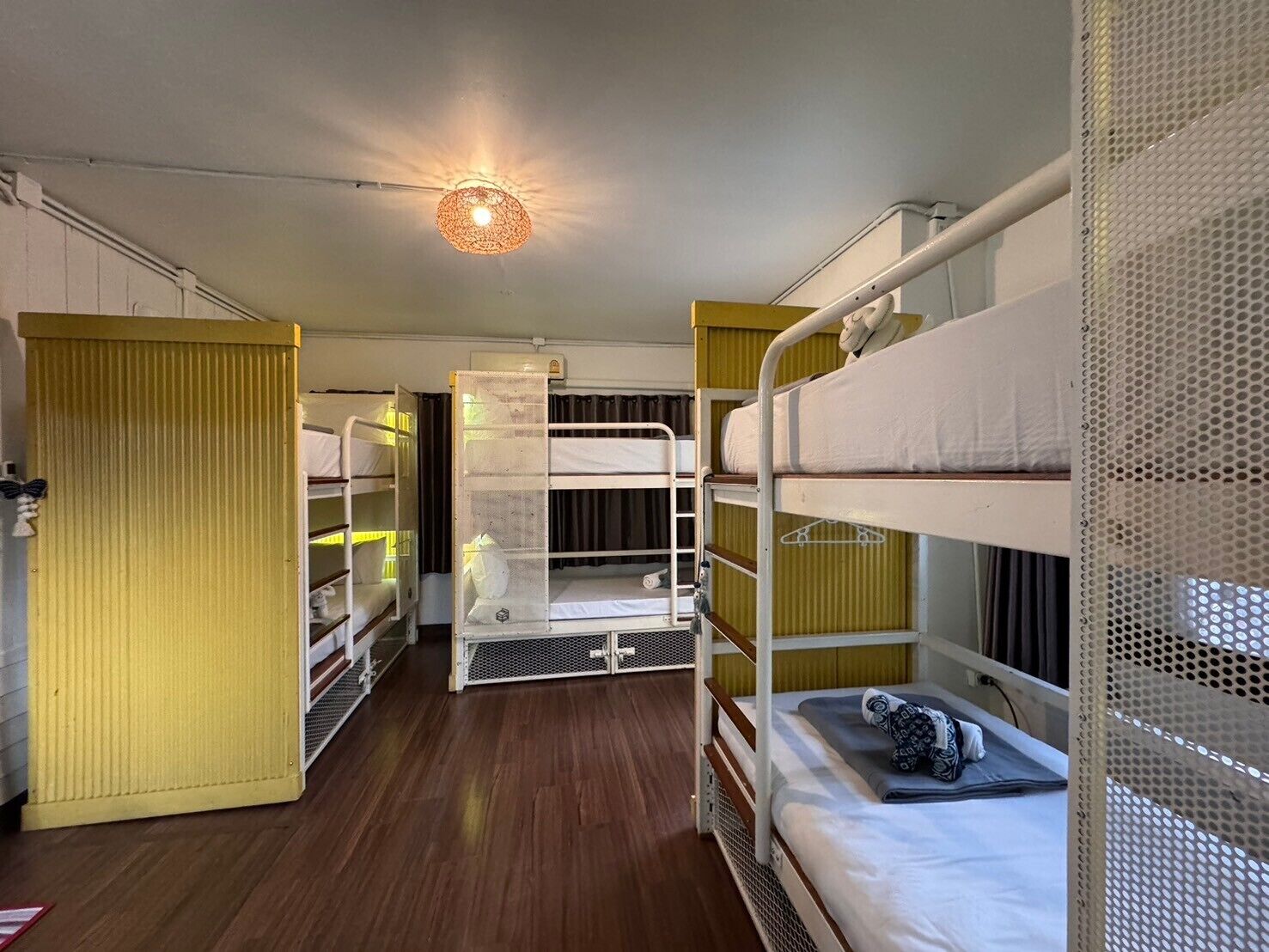 Quarto compacto com beliches, piso de madeira e luminária no teto.