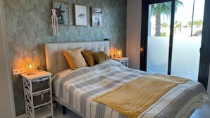 Ein Schlafzimmer mit einem großen Bett, zwei Nachttischen, einer Wanddeko aus Makramee und gerahmten Kunstwerken.