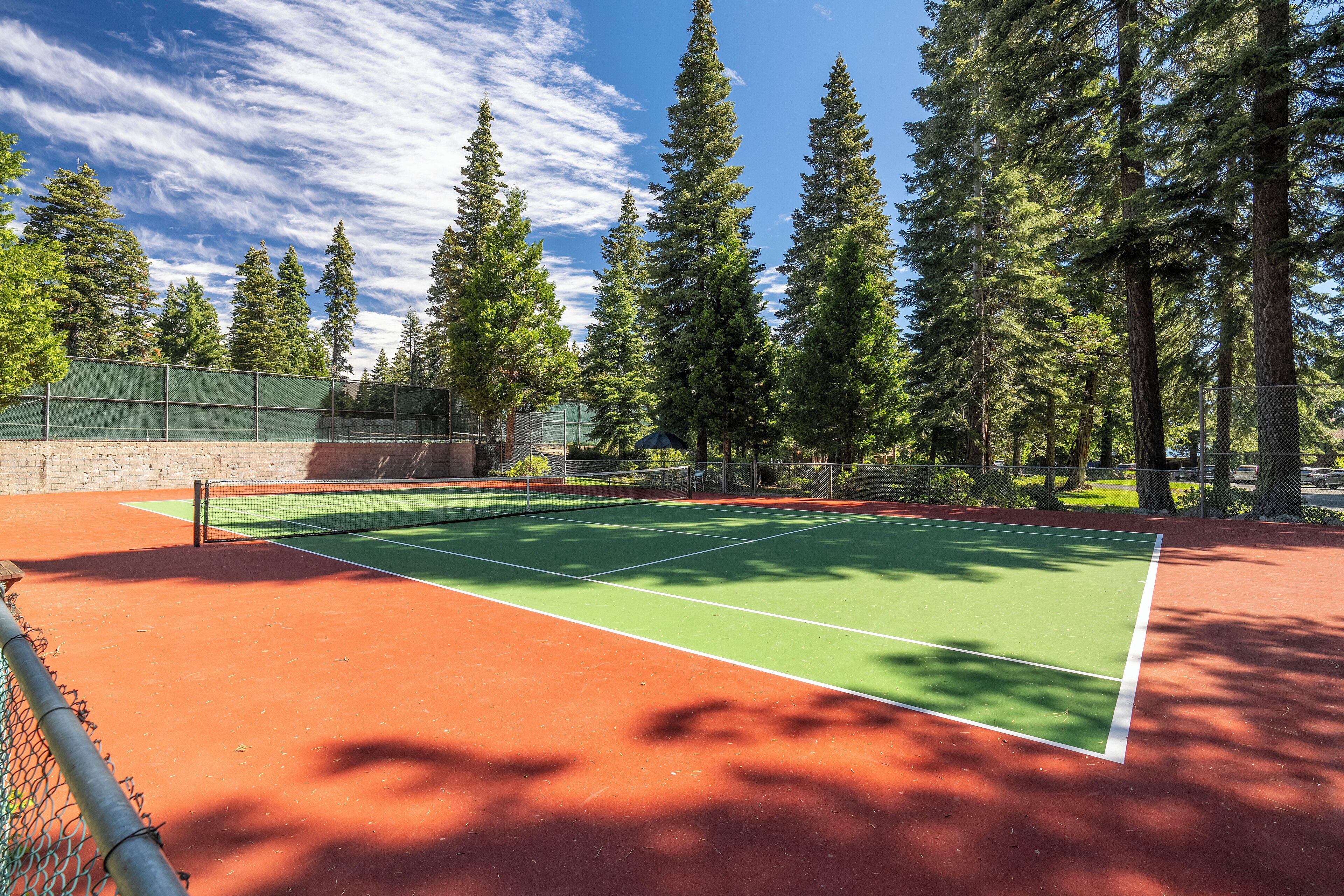 A tennis court with a net, surrounded by trees and a fence.