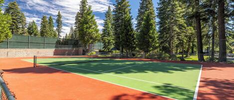 A tennis court with a net, surrounded by trees and a fence.