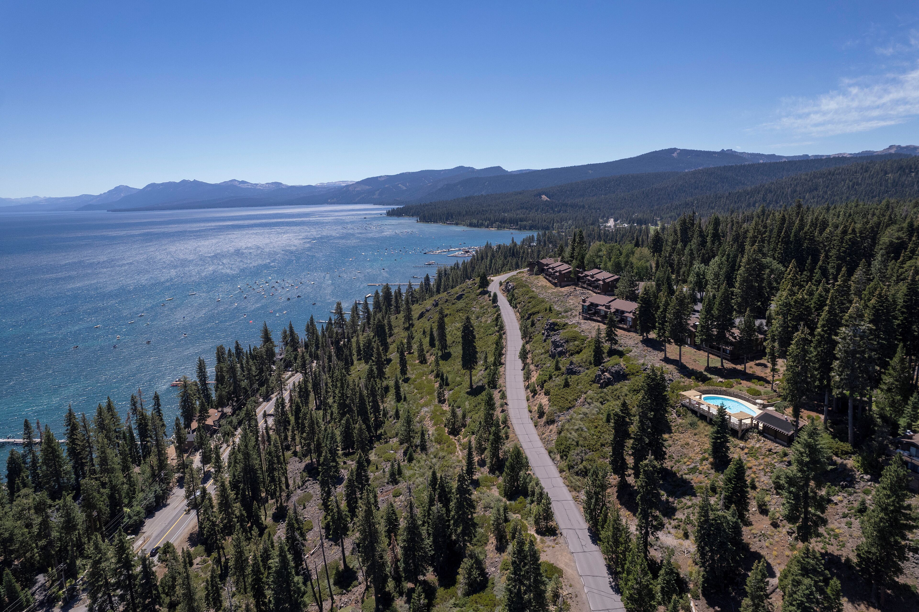 An aerial view of a coastal property with a swimming pool, surrounded by dense forest and mountains in the background.