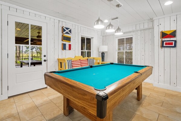 Een poolruimte met een pooltafel, een gele bank en vlaggen aan de muren.