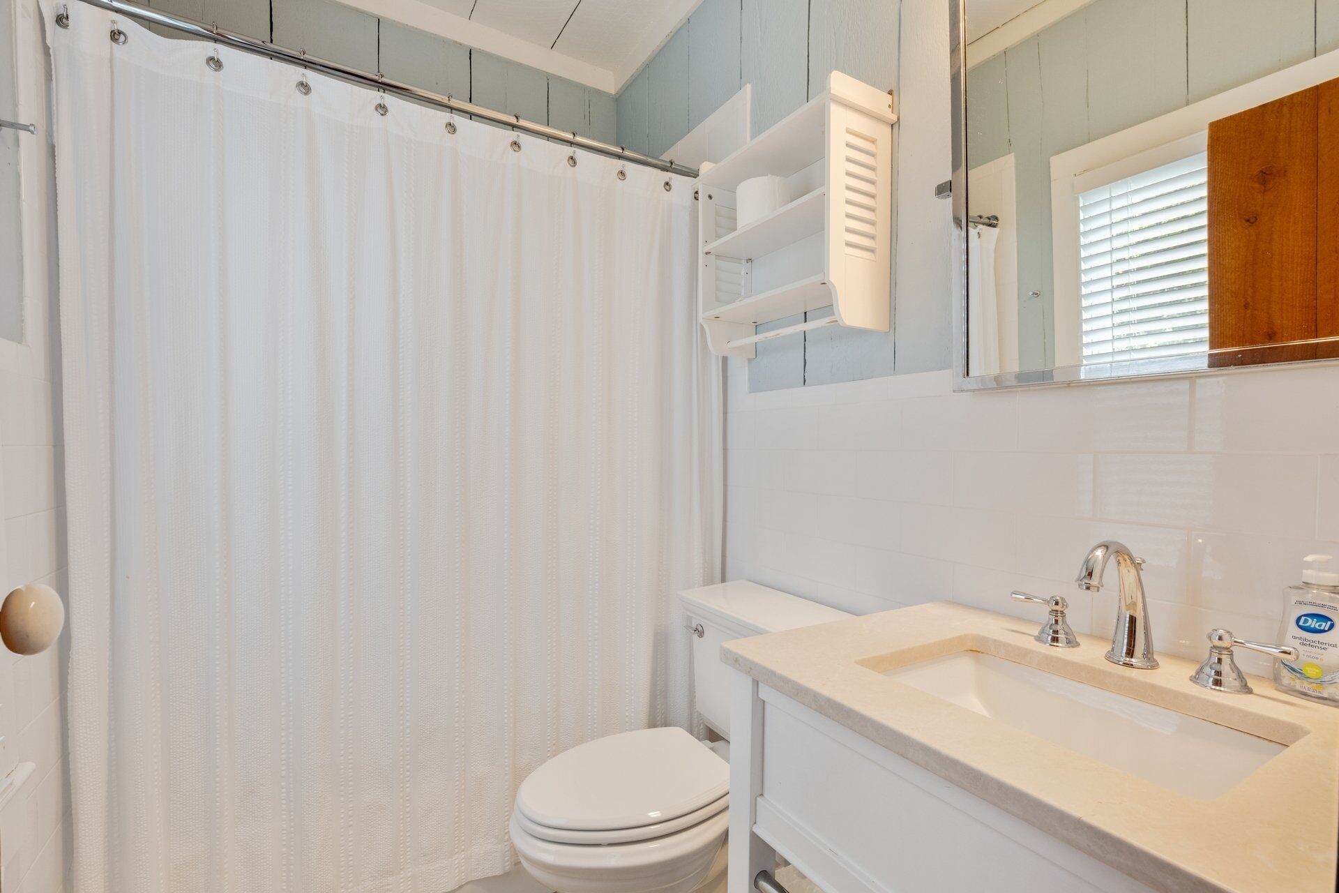 A bathroom with a shower curtain, toilet, sink, and mirror.