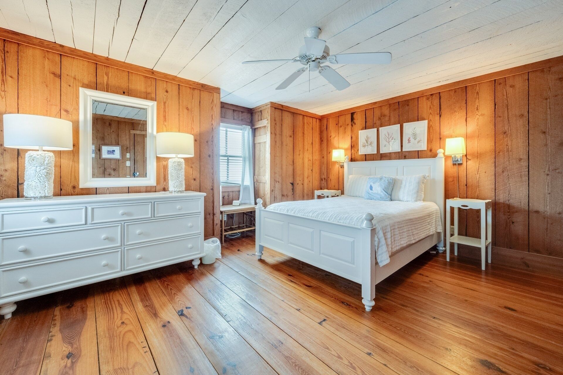Ein Schlafzimmer mit Holzwänden, einem weißen Bett, einem Schminktisch und einem Deckenventilator.