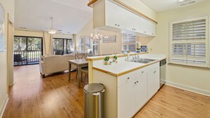 A modern kitchen with a central island, a dining area with a sofa and chairs, and a view of the outdoors through large windows.