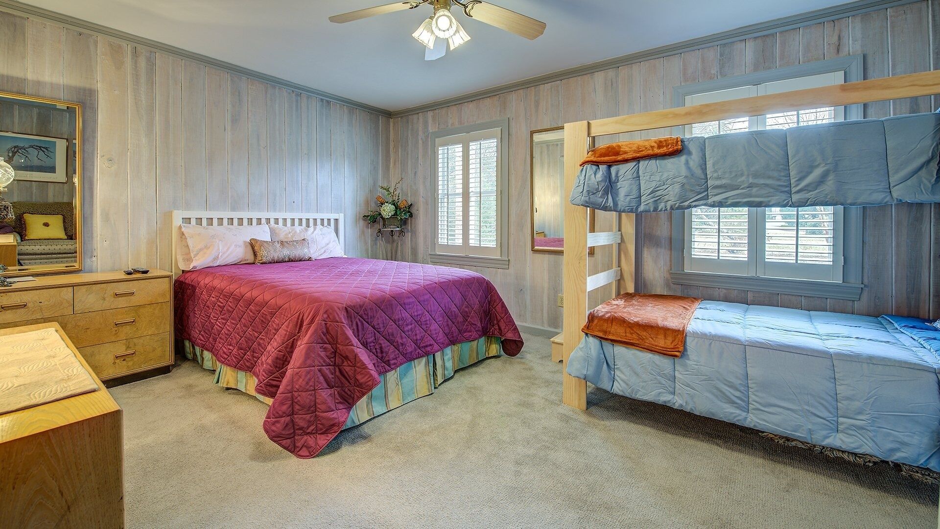 A bedroom with a bunk bed, a single bed, a dresser, and a ceiling fan.