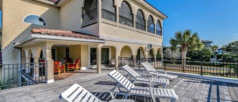 A resort with a covered outdoor seating area, a pool with lounge chairs, and a building with arches and balconies.