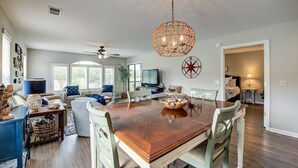 A spacious living room with a wooden dining table, comfortable seating, a television, and a decorative ceiling light. - Anchors Away In This Spacious And Beautiful Condo Overlooking Pond And 4th Hole 3 Bedroom Condo by Peace Vacations (Pawleys Island)