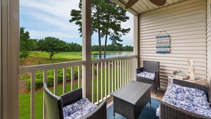 A covered outdoor seating area with wicker furniture and a view of a golf course and river. - Anchors Away In This Spacious And Beautiful Condo Overlooking Pond And 4th Hole 3 Bedroom Condo by Peace Vacations (Pawleys Island)
