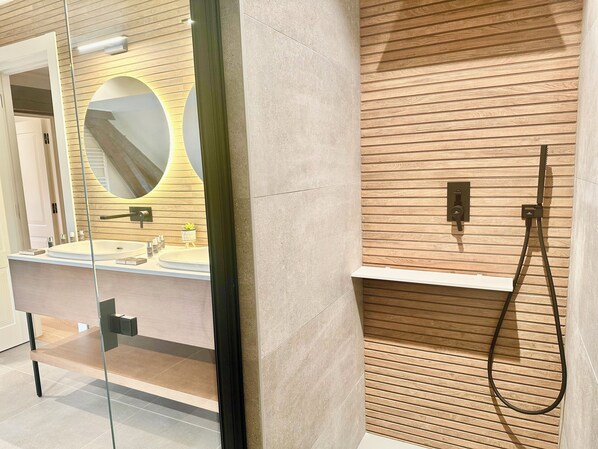 A modern bathroom with a wooden panel wall, a round mirror, a sink, and a handheld showerhead. - Les Rêveries du Clos - Hôtel Pommard (Pommard)