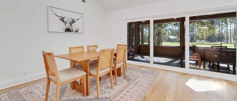 Un comedor con una mesa y sillas de madera, un tapete estampado y un ventanal con vistas a un parque.