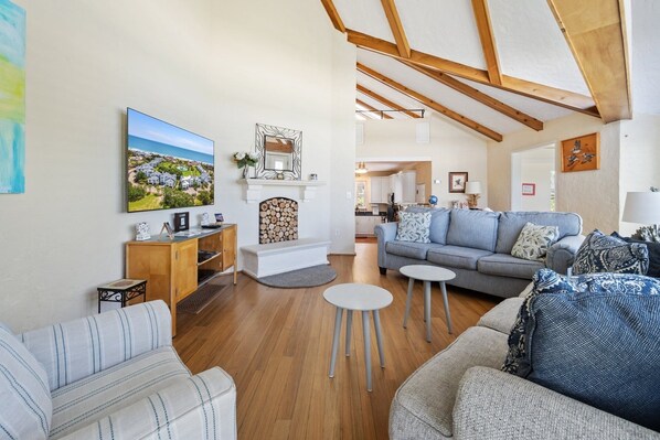 A spacious living room with a fireplace, a sofa set, a dining area, and a kitchen visible through an open door.