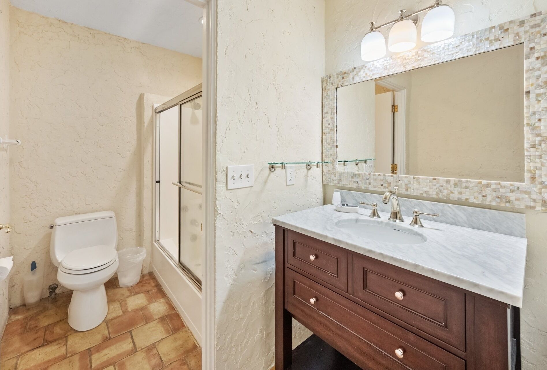 A bathroom with a white toilet, a glass shower enclosure, a marble sink, and a large mirror with mosaic tile detailing.