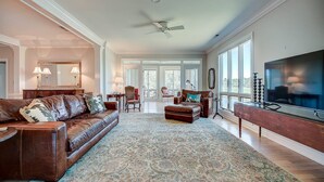 A spacious living room with a brown leather sofa, a patterned rug, a wooden coffee table, and a large flat-screen TV. - Looking For A Cozy Villa Located Next To The Golf Course? Good Trouble Is Your Answer! 3 Bedroom Villa by Peace Vacations (Georgetown)