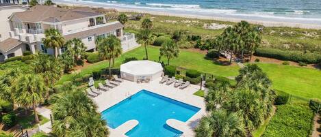 A pool area with a view of the ocean, surrounded by palm trees and a well-maintained lawn.