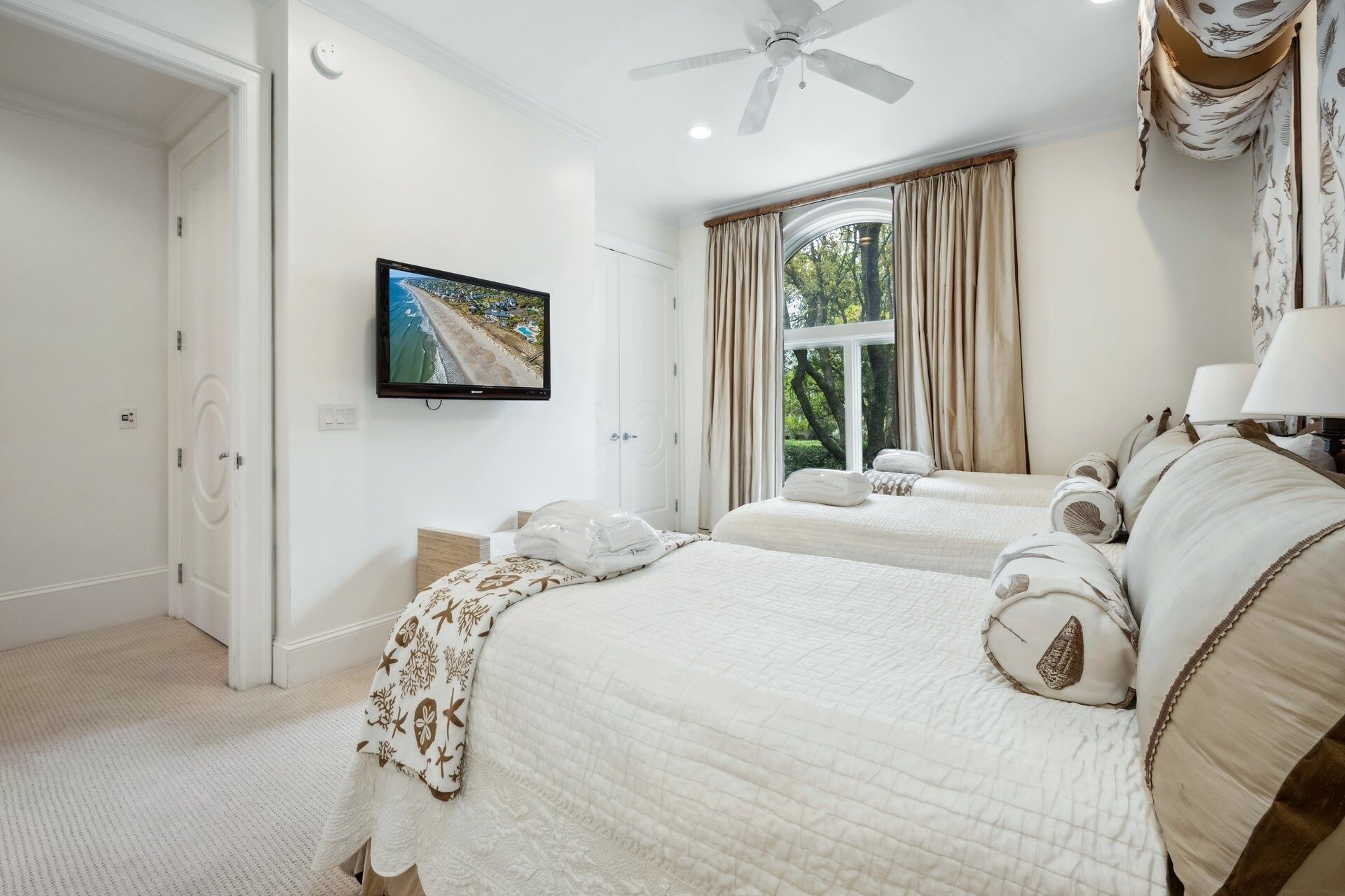 A hotel room with two beds, a ceiling fan, a TV, and a window with curtains.