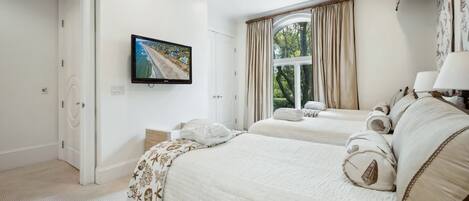 A hotel room with two beds, a ceiling fan, a TV, and a window with curtains.