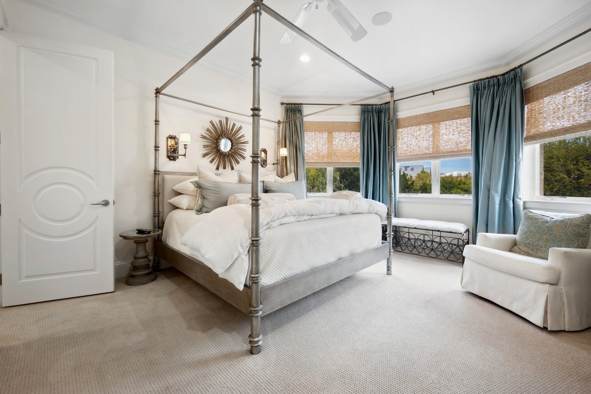 A bedroom with a four-poster bed, a daybed, a window with a view, and a small table with a lamp.