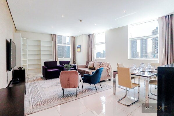 A modern living room with a sofa, chairs, a dining table, and a TV. - WelHome - Luxury Living in Business Bay 2BR + Maid's Room (Dubai)
