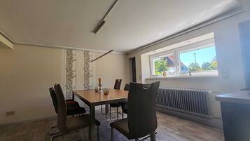 A modern dining room with a wooden table and chairs, a window with a view of the outside, and a radiator on the wall.