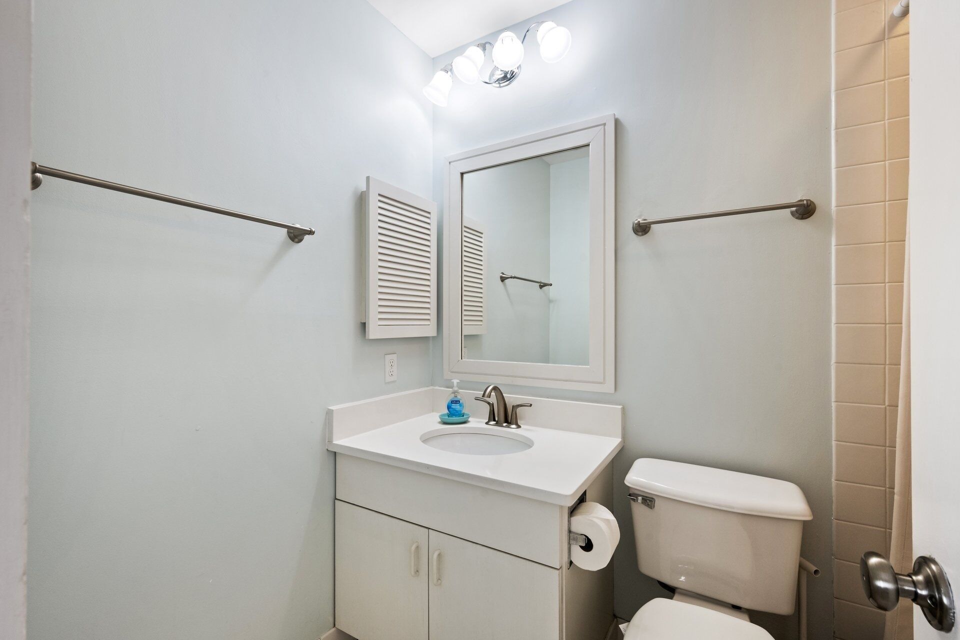 A bathroom with a toilet, sink, mirror, towel rack, and a shower area.