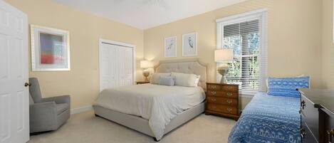 A bedroom with a bed, a chair, a dresser, a window with blinds, and a ceiling fan.