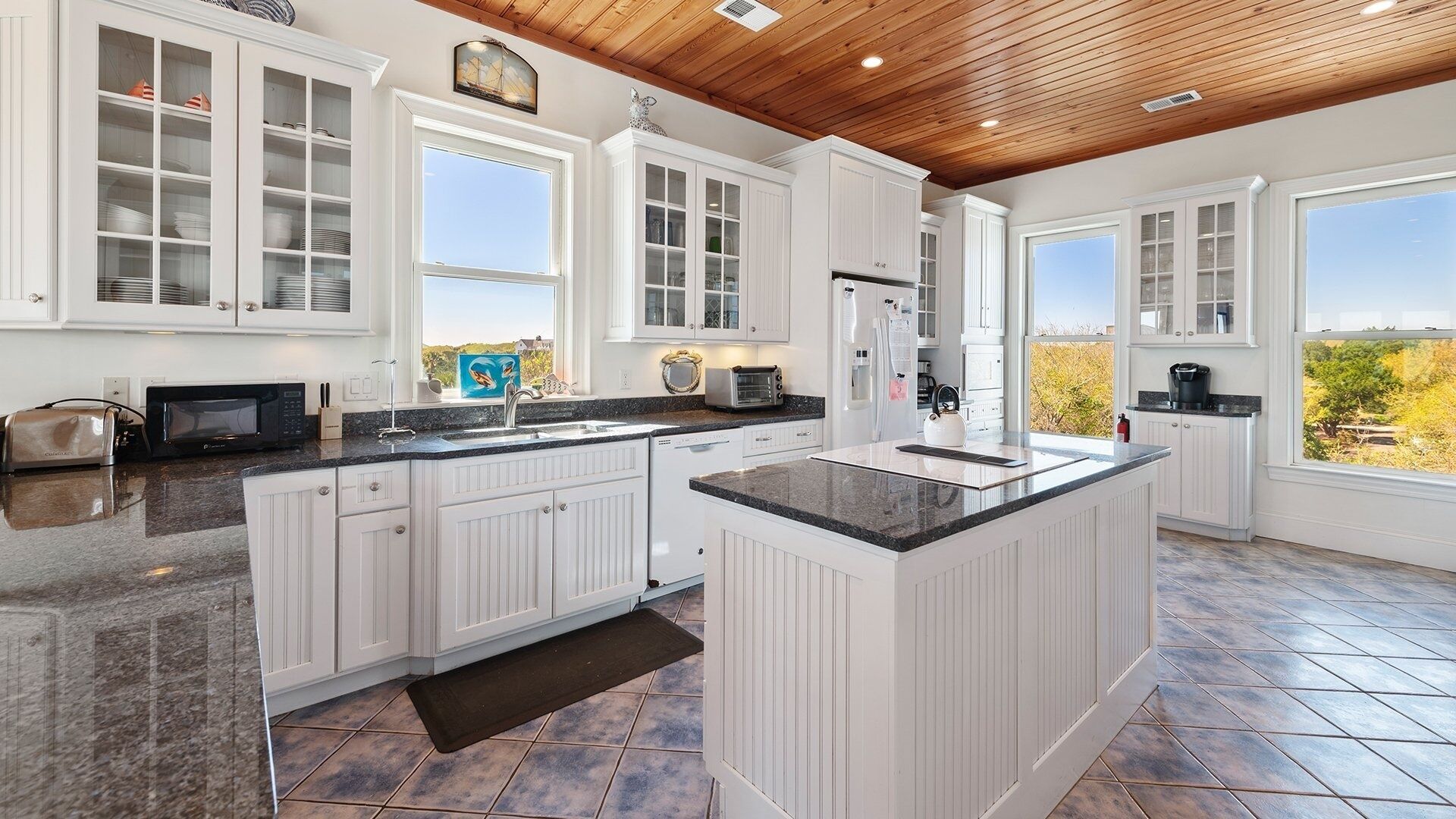 A spacious kitchen with white cabinetry, a large island, and a view of the outdoors.