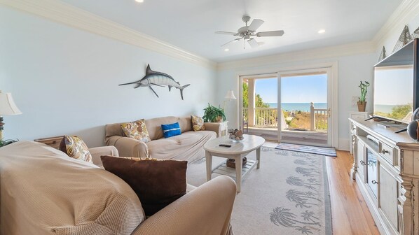 A living room with a sofa, coffee table, and a view of the ocean through a sliding glass door. - Out Of This World Beachfront Home 6 Bedroom Home by Peace Vacations (Georgetown)