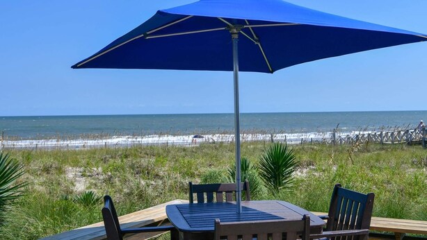 A beachside table with chairs and a blue umbrella, overlooking the ocean. - Par Fore The Course Offers A Home Away From Home Feel. 4 Bedroom Home by Peace Vacations (Georgetown)