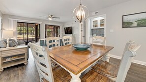 A dining room with a wooden table, white chairs, and a chandelier. - Golf Getaway, Special Event, Family Vacation Or Business Retreat 2 Bedroom Condo by Peace Vacations (Pawleys Island)