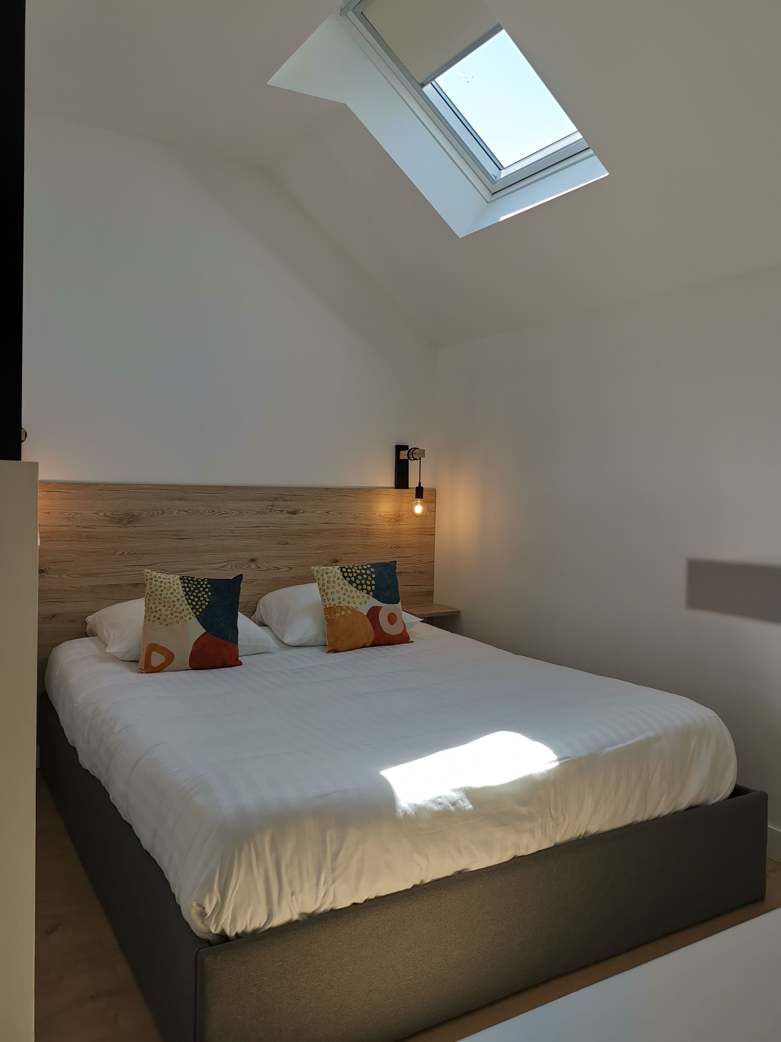 A bedroom with a skylight, a bed with white bedding, and a wooden headboard.