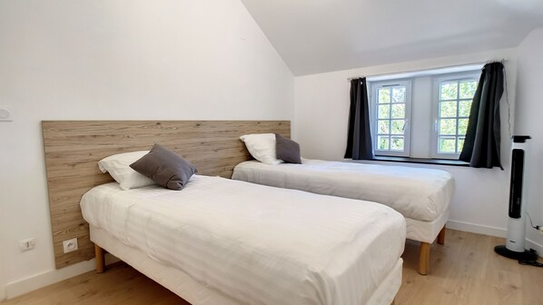 Een slaapkamer met twee enkele bedden, een houten hoofdbord, een raam met gordijnen en een radiator.