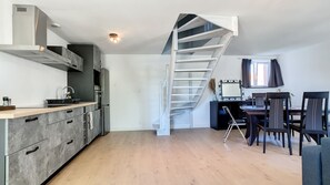 Une cuisine moderne dotée d’une cuisinière intégrée, un coin repas avec une table et des chaises, et un escalier en colimaçon menant à un niveau supérieur.