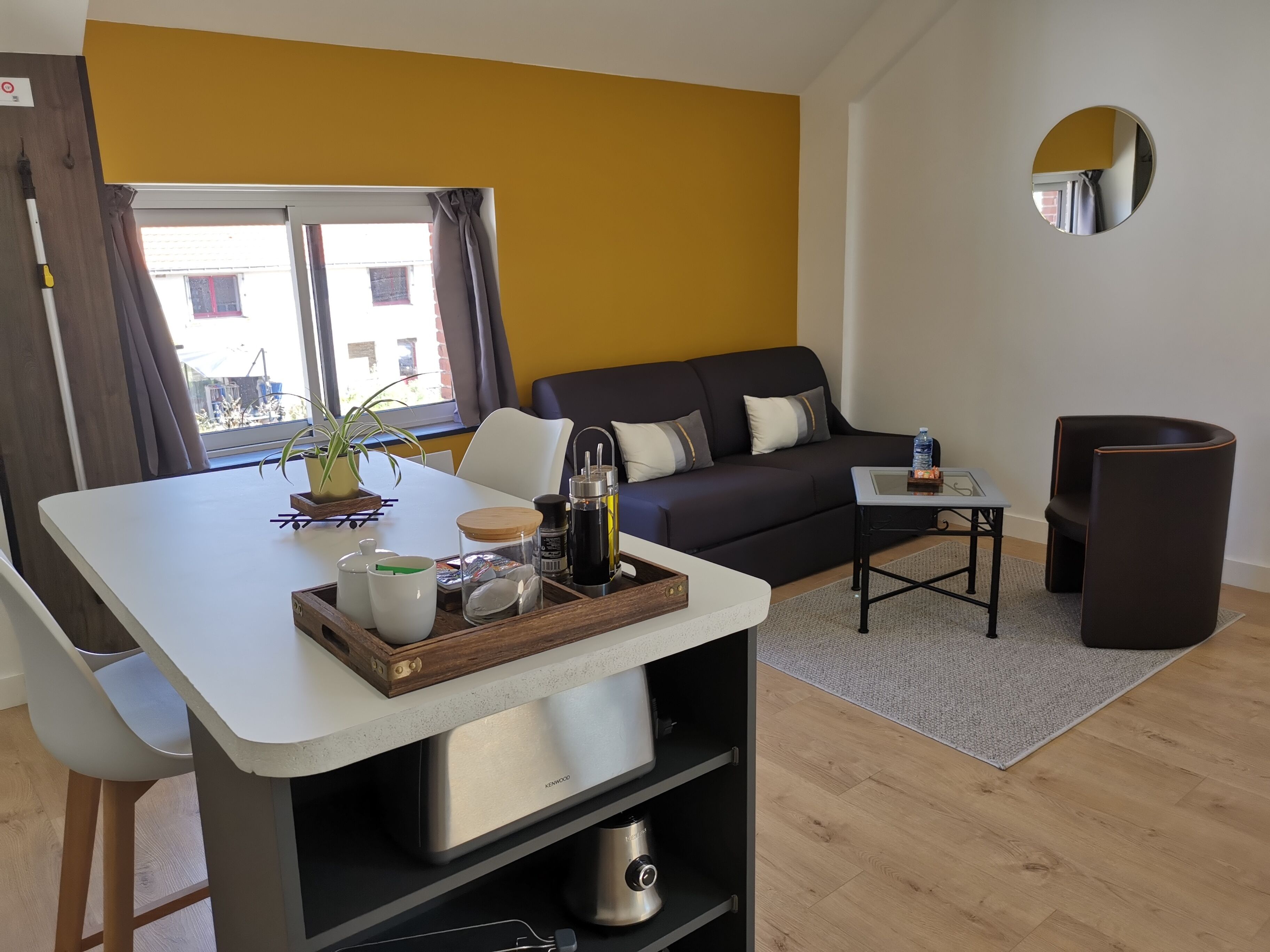 A modern living room with a sofa, a small table, a coffee table, and a kitchen area with a kettle and a kettle.