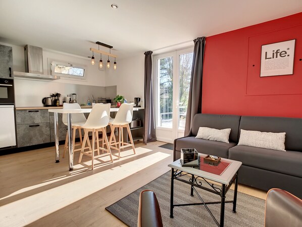 Un salon moderne avec un canapé gris, une table basse et un coin cuisine comprenant un ensemble de salle à manger.