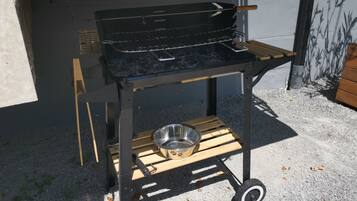 A portable grill with a metal bowl on a wheeled cart, set outdoors on gravel.